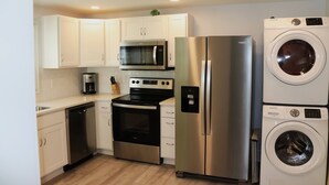 Cocina moderna con armarios blancos y electrodomésticos de acero inoxidable, incluyendo un microondas, horno, refrigerador y lavadora.
