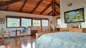 Una habitación con techo de madera, ventanas amplias, una cama, un escritorio y un cuadro.