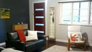 Ein Wohnzimmer mit dunkelblauer Wand, einer schwarzen Ledersofa mit roter Decke, einem weißen Sessel und einem Holzschrank.