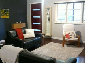 A living room with a dark blue wall, a black leather sofa with a red throw, a white armchair, and a wooden cabinet. - Dwellingup Escape. Large home opp Forest. Sleeps 8, 1.5 Bathrooms. Games Rm (Dwellingup)