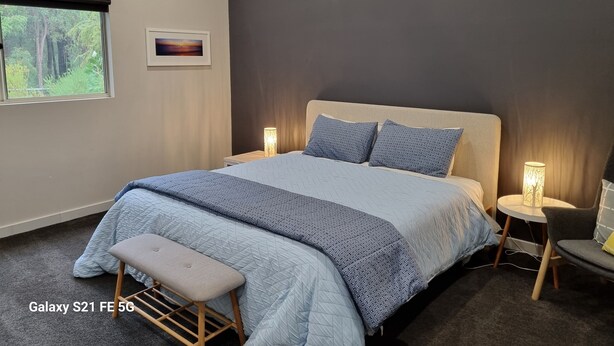 Ein modernes Schlafzimmer mit einem großen Bett, zwei Nachttischlampen, einer Bank und Blick ins Freie durch ein Fenster.