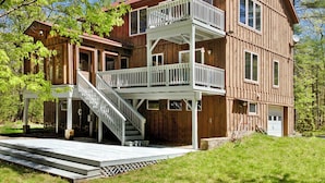 A two-story wooden cabin with a balcony on the upper floor, a covered porch, and a staircase leading to the entrance. - STUNNING  VACATION AND SKI HOME - Hudson Valley, Woodstock, Hunter (Palenville)