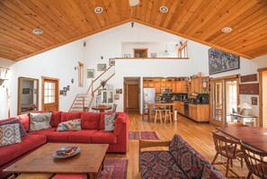 Ein großzügiger Wohnbereich mit einem roten Sofa, einem Holzespeisesaal und einer Küche mit Holzschränken und hohen Decken.