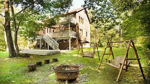 A rustic wooden house with a porch, a swing set, and a fire pit in the yard. - STUNNING  VACATION AND SKI HOME - Hudson Valley, Woodstock, Hunter (Palenville)