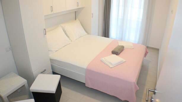 A neatly made bed with a pink bedspread, a rolled towel, and a white pillow. - Danica - apartment 003 (Promajna)