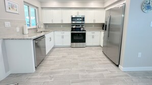 Una cucina moderna con mobili bianchi, elettrodomestici in acciaio inossidabile e pavimento in piastrelle a spina di pesce.