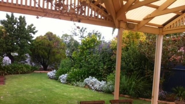 A wooden pergola with a table and chairs in a garden setting.