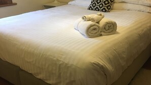 A neatly made bed with white linens and rolled towels placed on top.