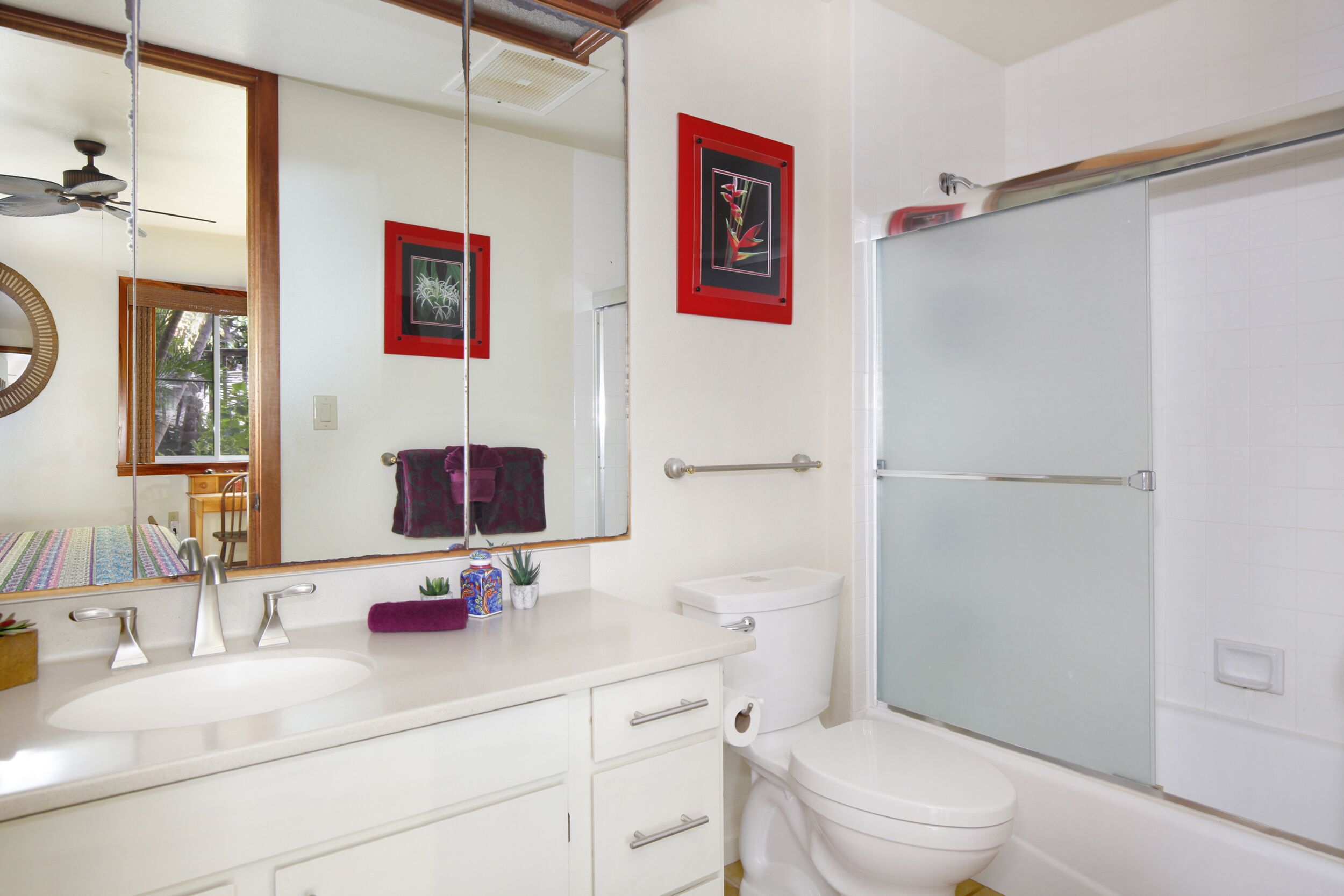 A bathroom with a white sink, a toilet, a shower with a glass door, a mirror, and a framed picture on the wall.