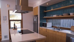 A modern kitchen with a central island, stainless steel appliances, and blue-tiled backsplash. - Camelot - opposite the foreshore. Stunning sea views. (Kingscote)