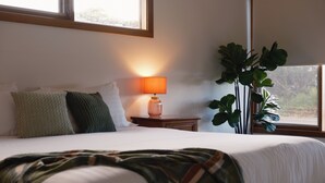 A neatly made bed with a blanket, a bedside lamp, and a potted plant in a room with a window. - Camelot - opposite the foreshore. Stunning sea views. (Kingscote)
