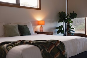 A neatly made bed with a blanket, a bedside lamp, and a potted plant in a room with a window.