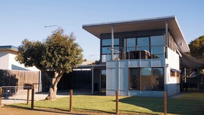 A modern building with large windows, a flat roof, and a tree in the foreground. - Camelot - opposite the foreshore. Stunning sea views. (Kingscote)