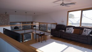 A modern living room with a sofa, a dining table, and a view of the outside through large windows. - Camelot - opposite the foreshore. Stunning sea views. (Kingscote)