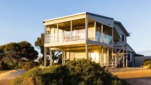 Une maison moderne à deux étages, dotée d’un balcon, et entourée d’un paysage naturel et d’arbres.