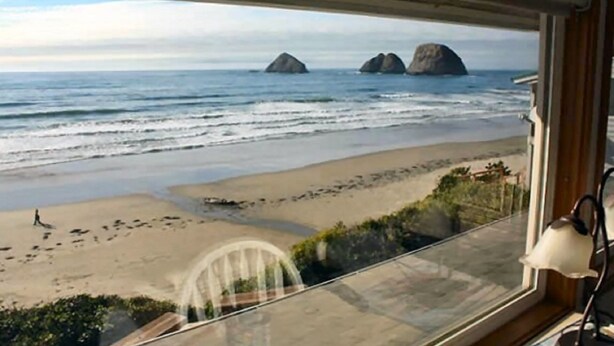 Vista desde una habitación con un amplio ventanal que da a una playa y tres grandes formaciones rocosas en el agua.