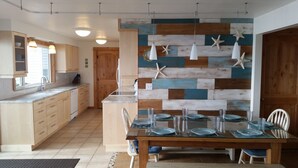 Una cocina moderna con armarios de madera, una isla central y un comedor con una mesa de vidrio para cuatro.