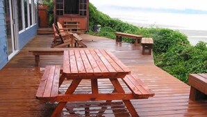 Una terraza de madera con mesas de picnic y bancos, con vista a un cuerpo de agua.