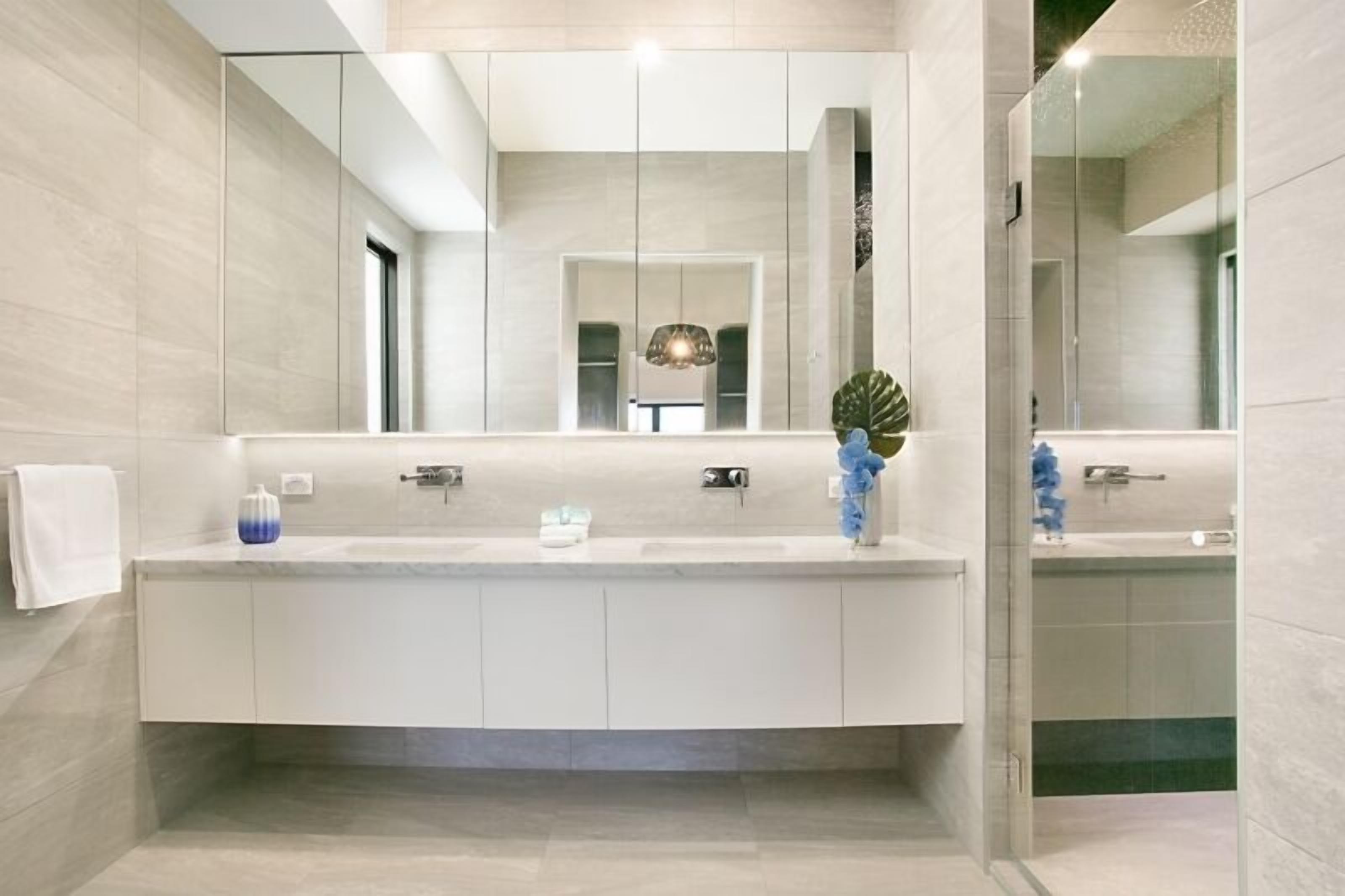 Une salle de bain moderne avec un grand miroir, deux lavabos et un espace douche.
