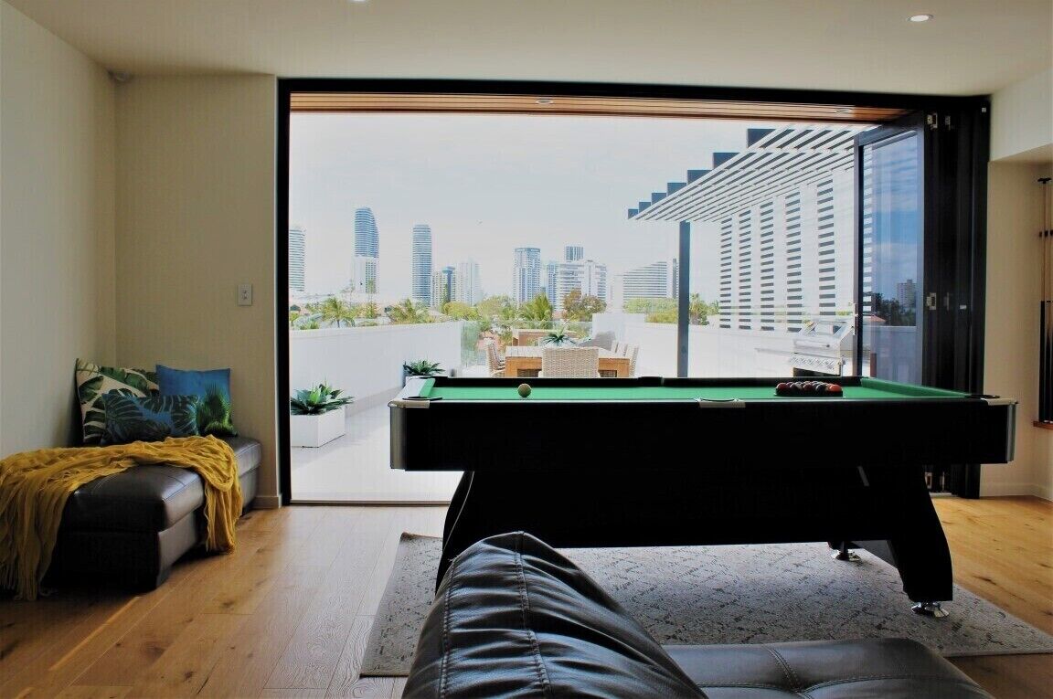 A modern living room with a pool table, a sofa, and a view of a cityscape through large windows.