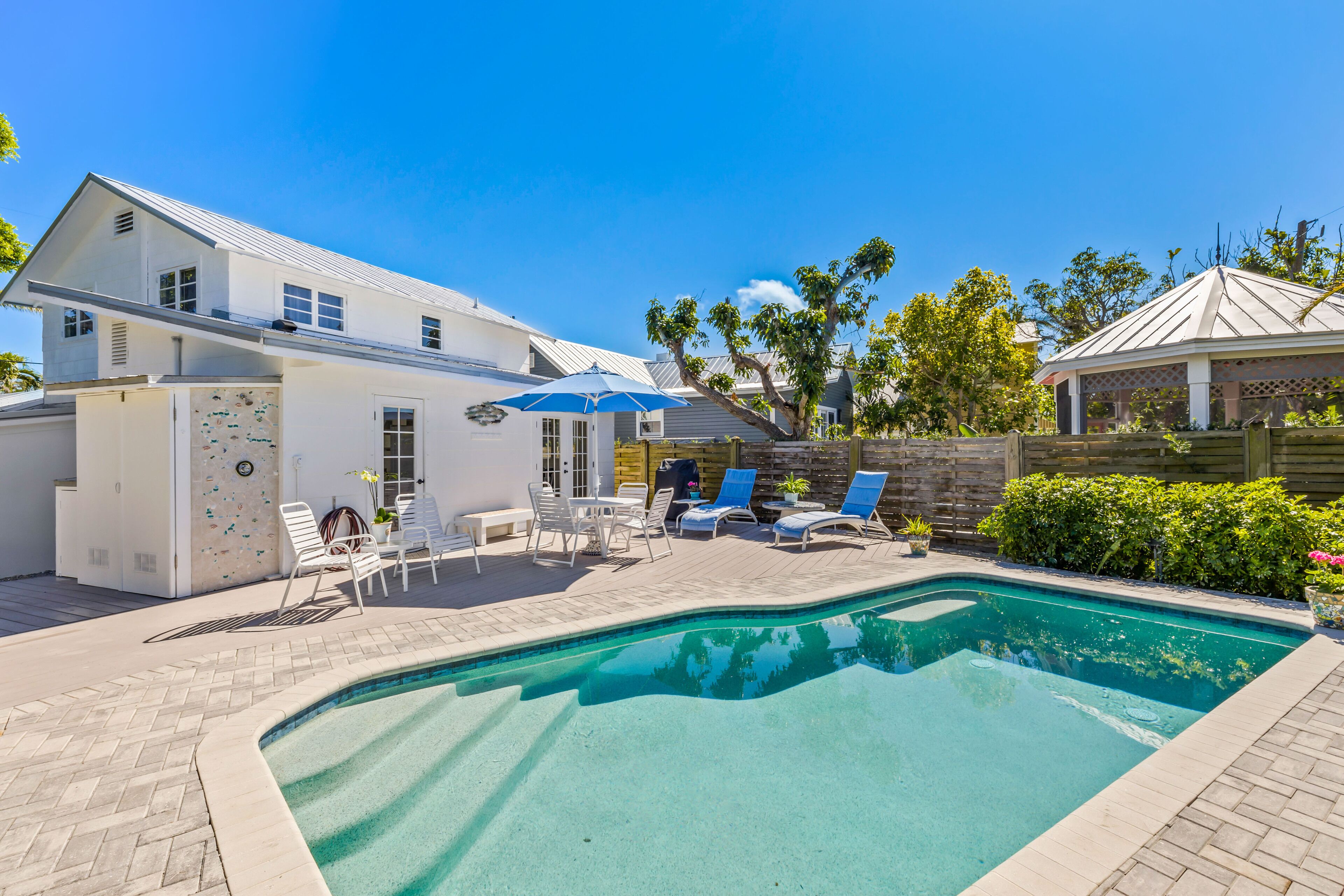 A backyard with a swimming pool, lounge chairs, and a covered patio area.