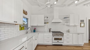 A modern kitchen with white cabinetry, a central island, a stove, and a ceiling fan.