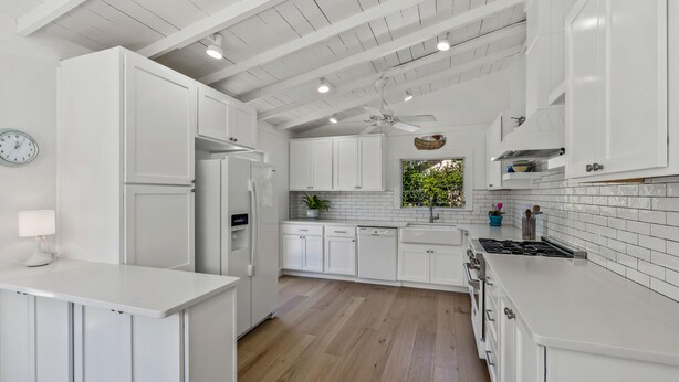 A modern kitchen with white cabinetry, a built-in oven, and a window with a view of greenery.