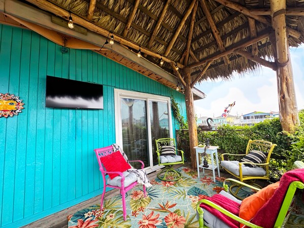 A turquoise building with a thatched roof, a large window, and a colorful floral rug. - Unique charming coastal cottage (Surfside Beach)