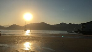 A beach with boats, a clear sky, and mountains in the background.