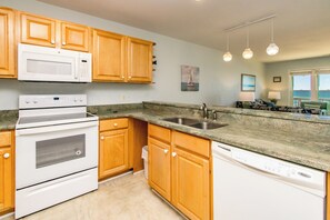 A kitchen with wooden cabinets, a microwave, an oven, a dishwasher, and a granite countertop.