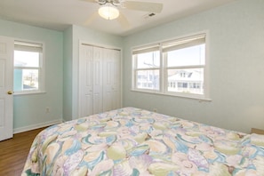 Quarto com cama, duas janelas, ventilador de teto e uma porta.