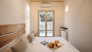 A bedroom with a wooden headboard, a bed with white linens, a breakfast tray on the bed, and a stone wall visible through the window.