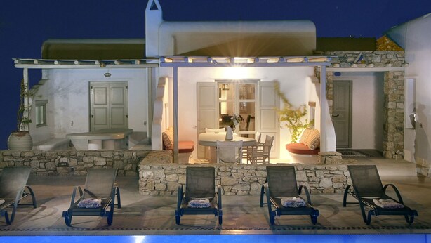 A building with a pool, lounge chairs, and a stone facade.