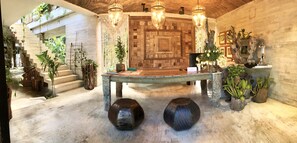 A rustic interior with a wooden table, hanging plants, and a stone wall with intricate patterns.