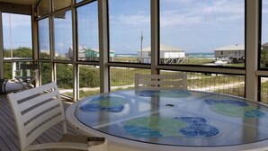 A covered outdoor area with a round table and chairs, large windows offering views of the ocean and houses. - Great Gulf Views and easy walk to the beach.  Dog Friendly! (Gulf Shores)