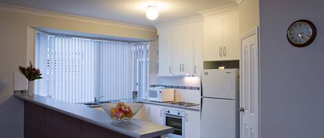A compact kitchen with white cabinets, a built-in oven, a microwave, and a refrigerator.