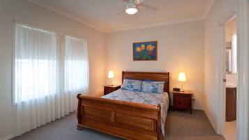 Une chambre à coucher avec un lit en bois, deux tables de chevet avec des lampes, un ventilateur de plafond et une fenêtre avec des rideaux légers.
