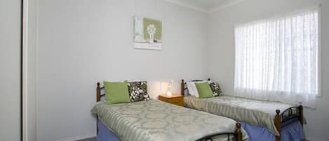 A bedroom with two single beds, a nightstand, a lamp, and a window with sheer curtains.