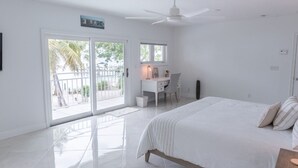Ein Schlafzimmer mit Bett, Schreibtisch und Stuhl. Ein Balkon bietet Blick auf Palmen.