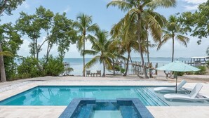 Ein Pool mit gefliestem Sonnendeck, umgeben von Palmen und Blick aufs Meer.