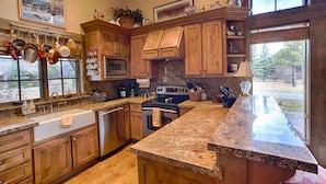 A spacious kitchen with wooden cabinets, granite countertops, a large island, stainless steel appliances, and a view of the outdoors. - Charming Jackson Hole cabin bordering Grand Teton National Park (Jackson)