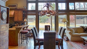 A spacious dining area with a wooden table and chairs, a kitchen with wooden cabinets, and large windows allowing natural light. - Charming Jackson Hole cabin bordering Grand Teton National Park (Jackson)