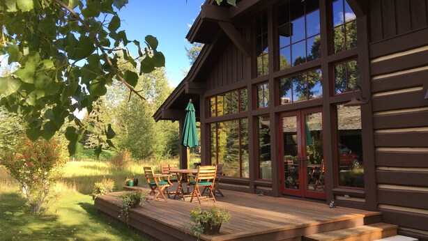 A wooden cabin with a deck, large windows, and outdoor seating. - Charming Jackson Hole cabin bordering Grand Teton National Park (Jackson)