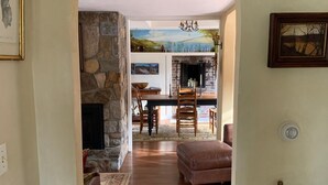 A cozy living room with a fireplace, a dining area with a stone wall, and a hallway leading to a kitchen.