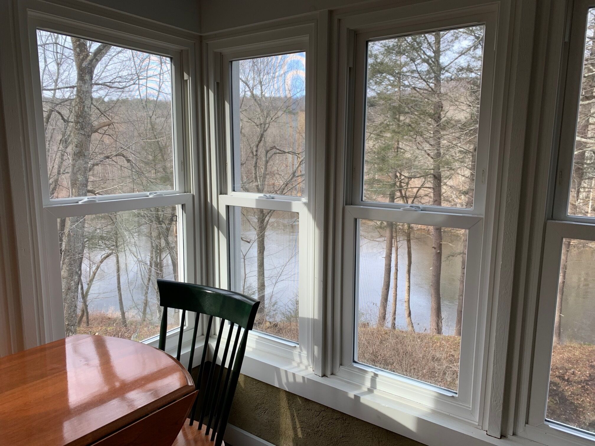 A room with a view of a lake and trees through large windows.