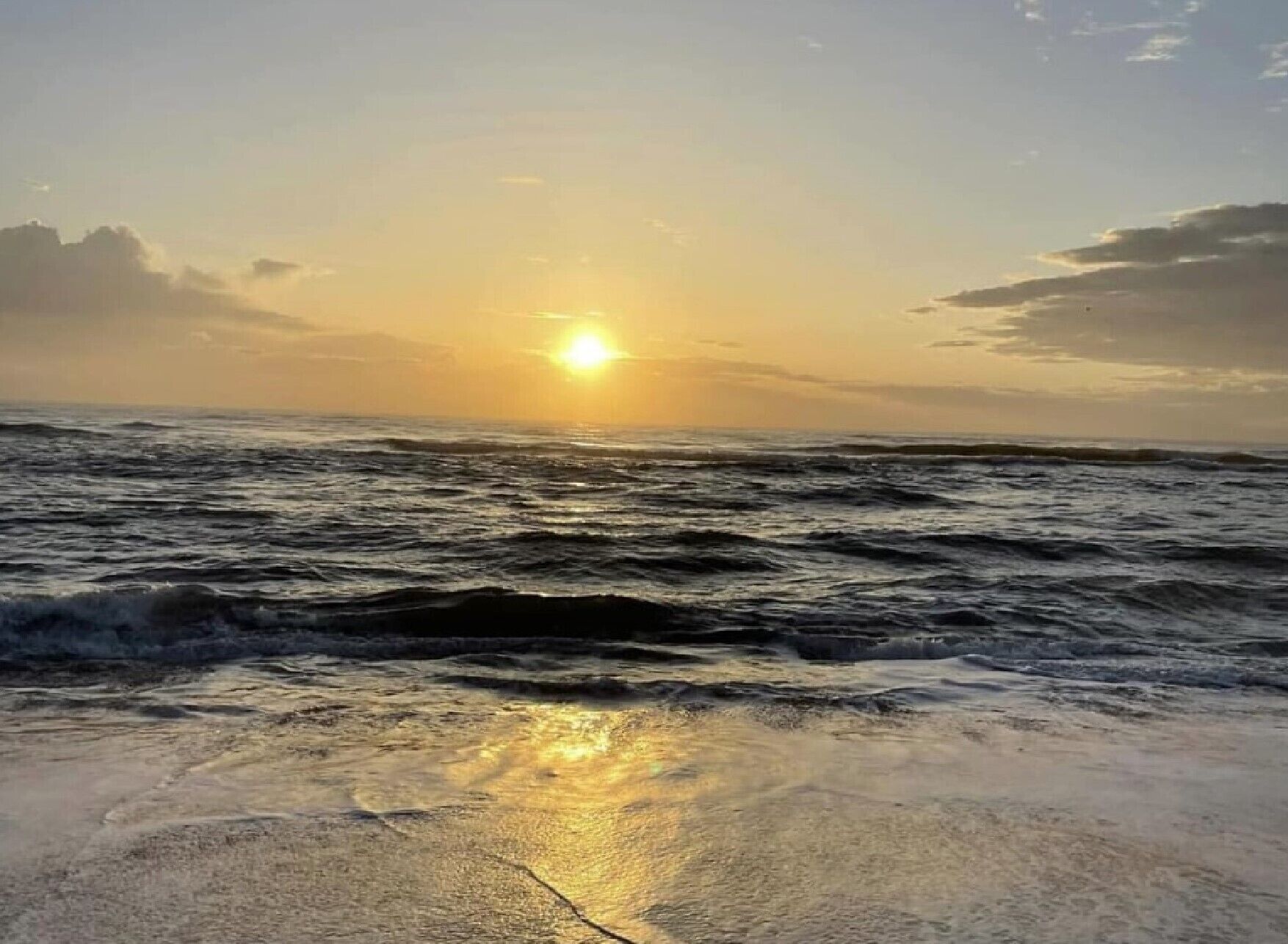 A beach with waves and a sunset.