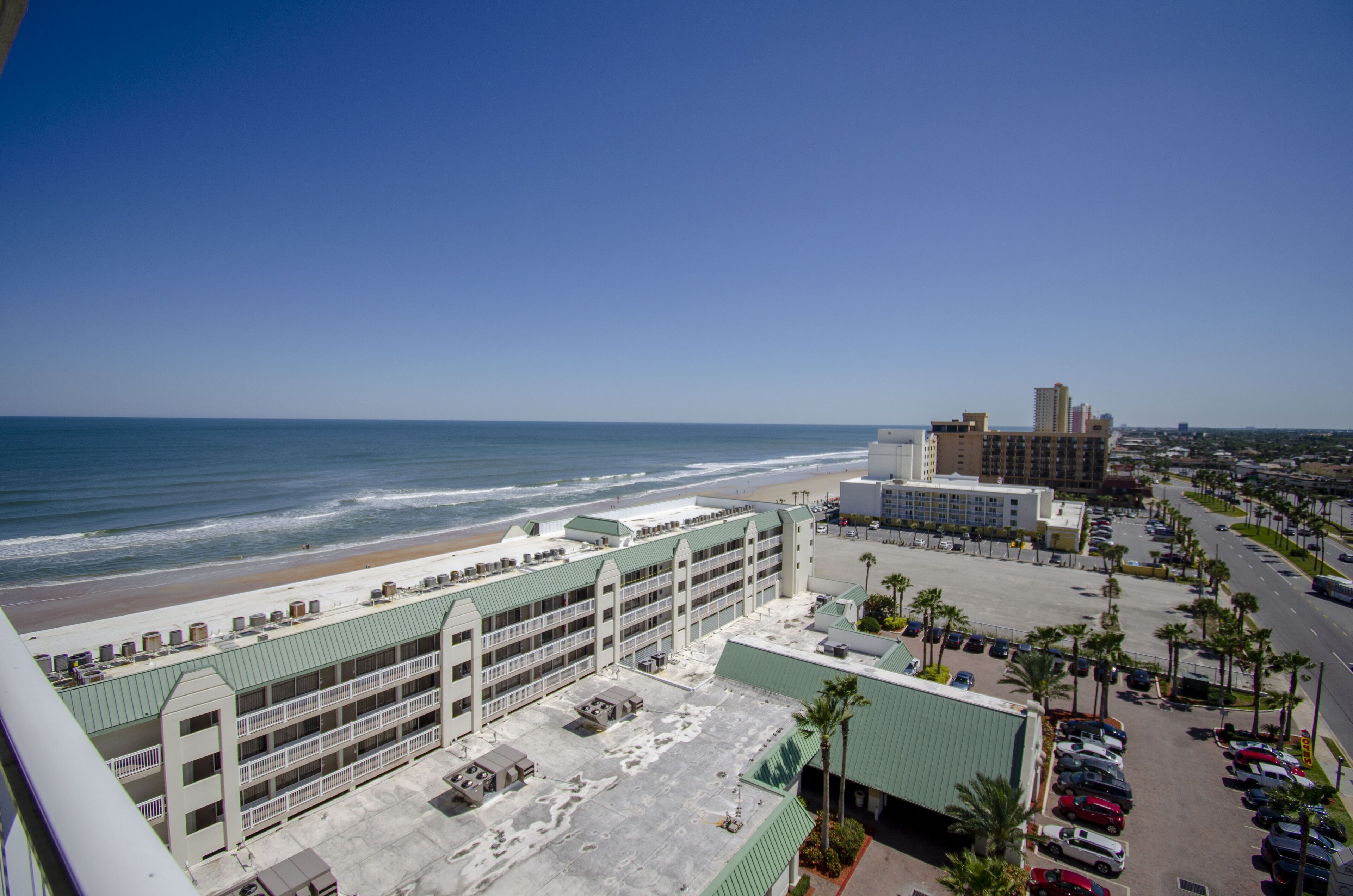 Ein Küstenhotel mit Parkplatz, Blick auf den Strand und einem großen Gebäude im Hintergrund.