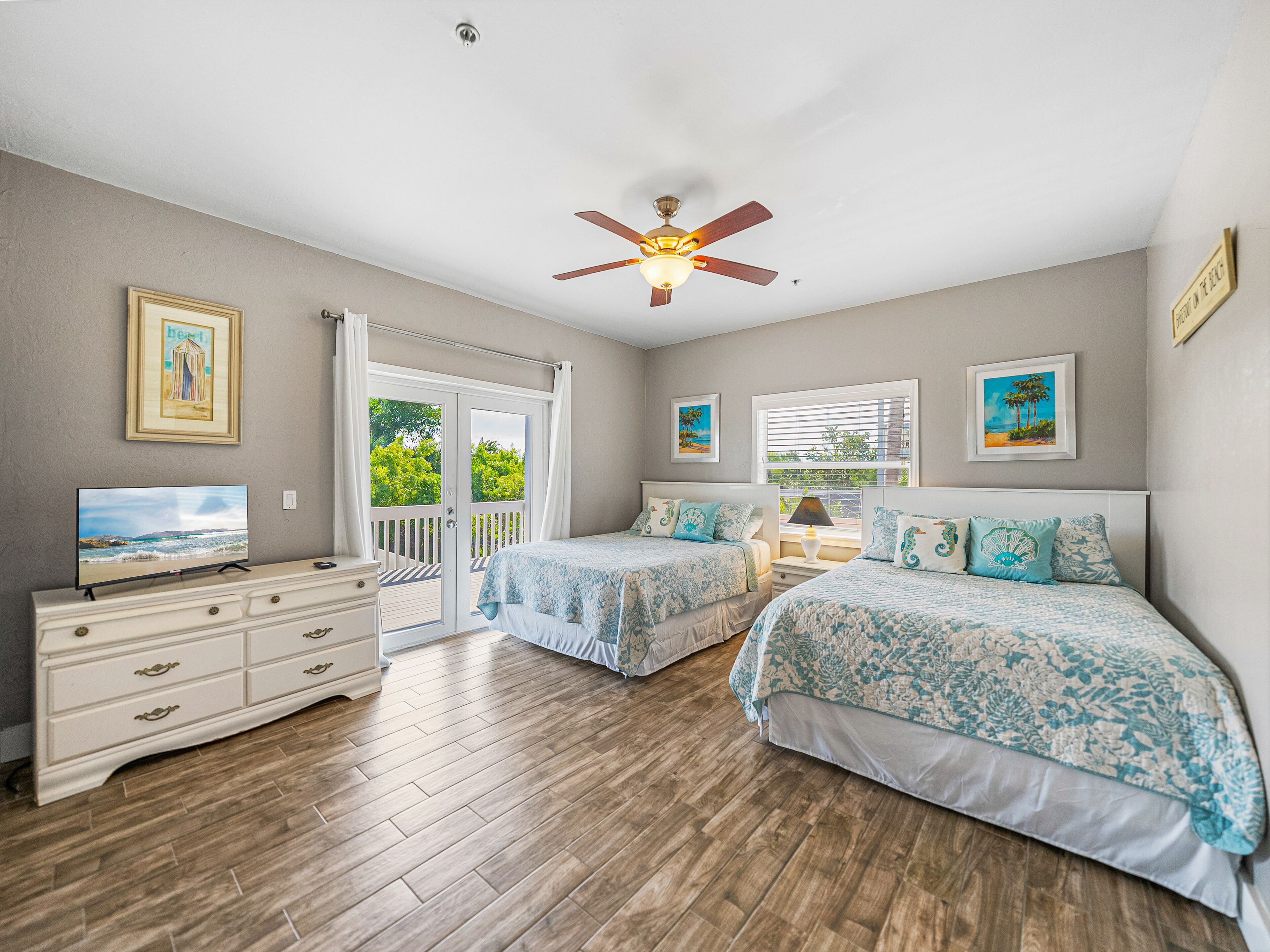 A bedroom with two beds, a TV, a dresser, and a ceiling fan.