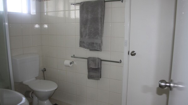 Un baño con un inodoro, un perchero con dos toallas y un dispensador de papel higiénico.
