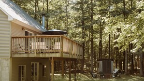 A wooden deck with chairs and a table, a small shed, and a house with a chimney. - Cedar Point Cottage- Perfect Lake Michigan Retreat (Mears)